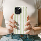 A person is holding a phone with a green and white striped case in front of them.