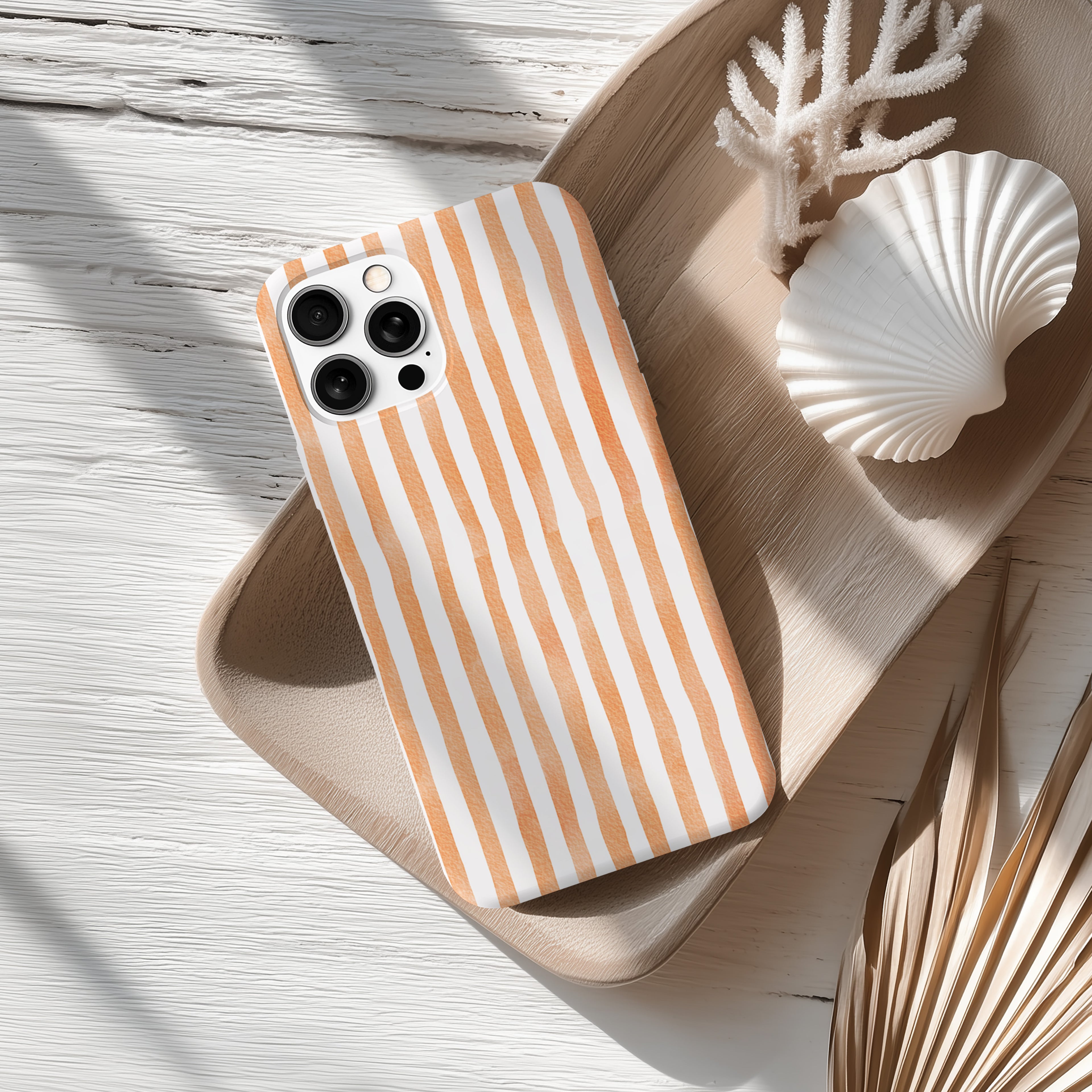 a smartphone with a striped case, placed on a wooden surface alongside a seashell and some dried leaves.