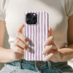 A person is holding a phone with a purple and white striped case in their hands.