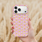 A hand holding a pink and white checkered phone case with yellow lemons printed on it, against a blurred background of wheat or straw.