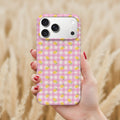 A hand holding a pink and white checkered phone case with yellow lemons printed on it, against a blurred background of wheat or straw.