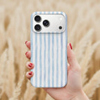 A hand holding a smartphone with a blue and white striped patterned case, against a blurred background of a field.
