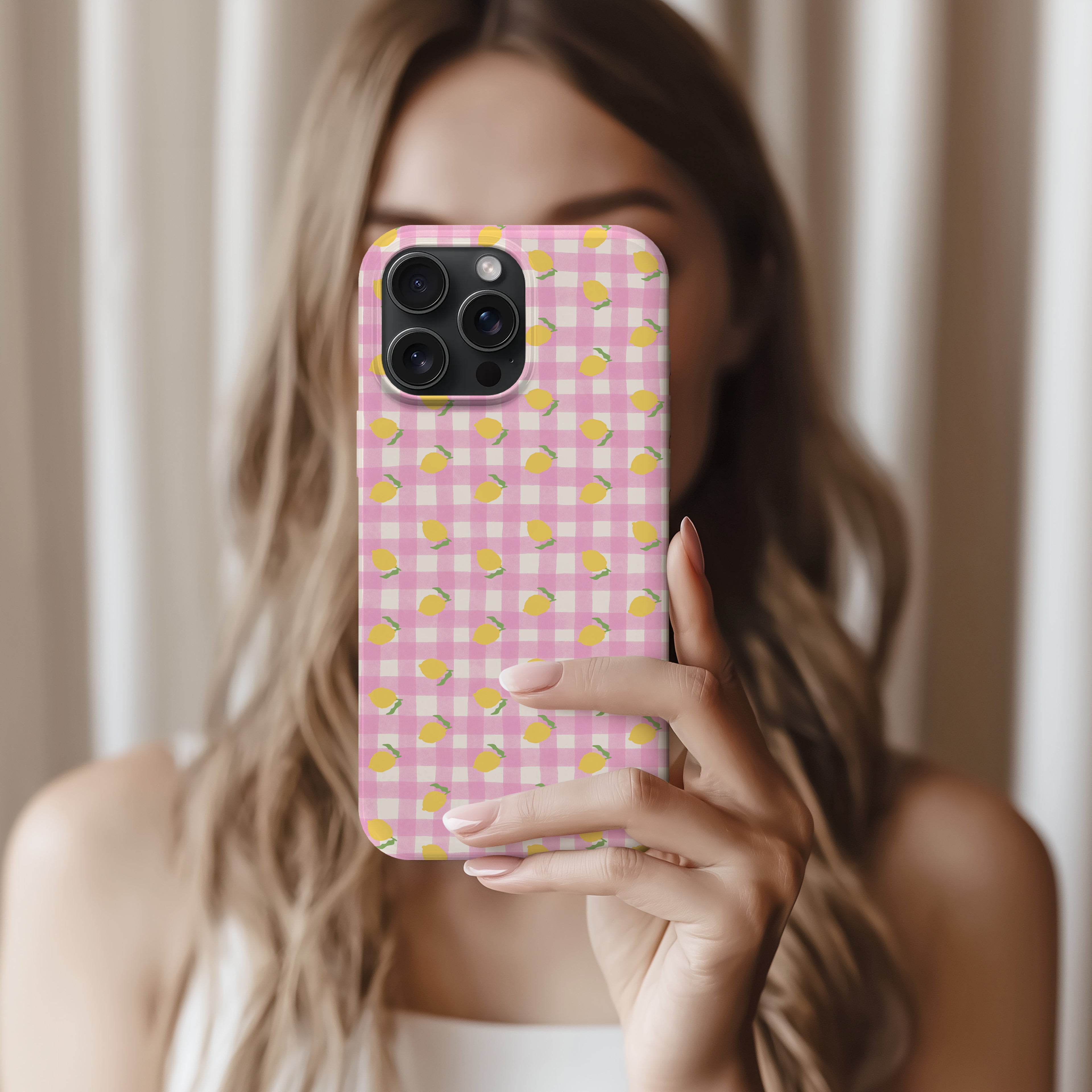 A woman is holding a pink and yellow checkered phone case and taking a selfie.