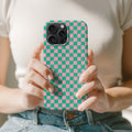 A person is holding a phone with a checkered pattern case, wearing a white shirt and blue jeans.