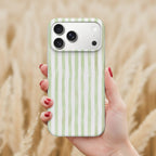 A hand holding a smartphone with a green and white striped patterned case, against a blurred background of a field.