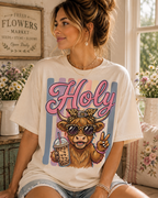 A woman wearing a white t-shirt with a graphic of a cow wearing sunglasses and holding a drink, with the word "Holly" written above it.