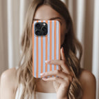 A woman with long, wavy hair is holding a smartphone with a striped pattern on the case, taking a selfie.