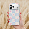 A hand holding a smartphone with a patterned case featuring blue and white stripes and pink star shapes.
