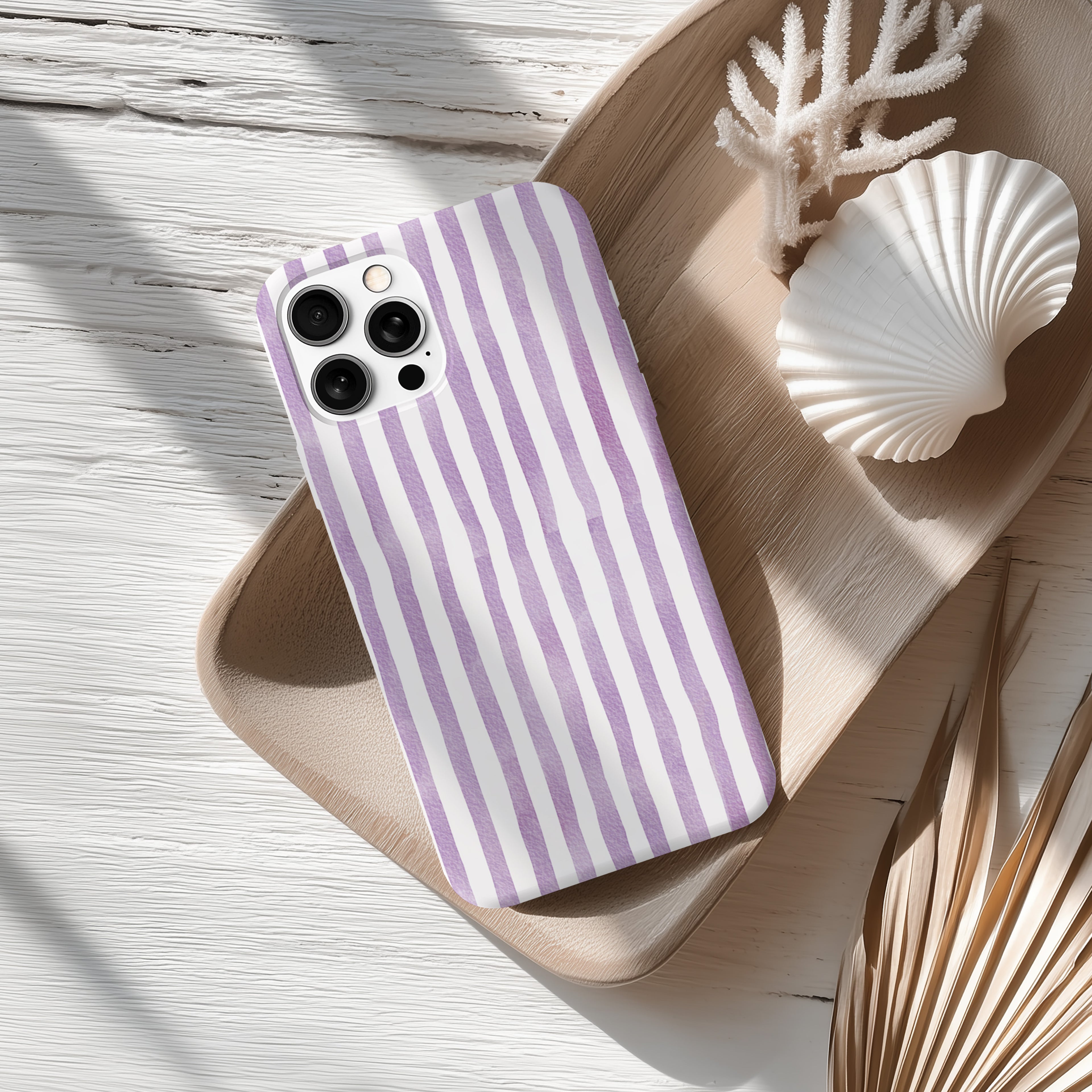 a purple and white striped phone case resting on a wooden surface, accompanied by a seashell and some dried leaves.