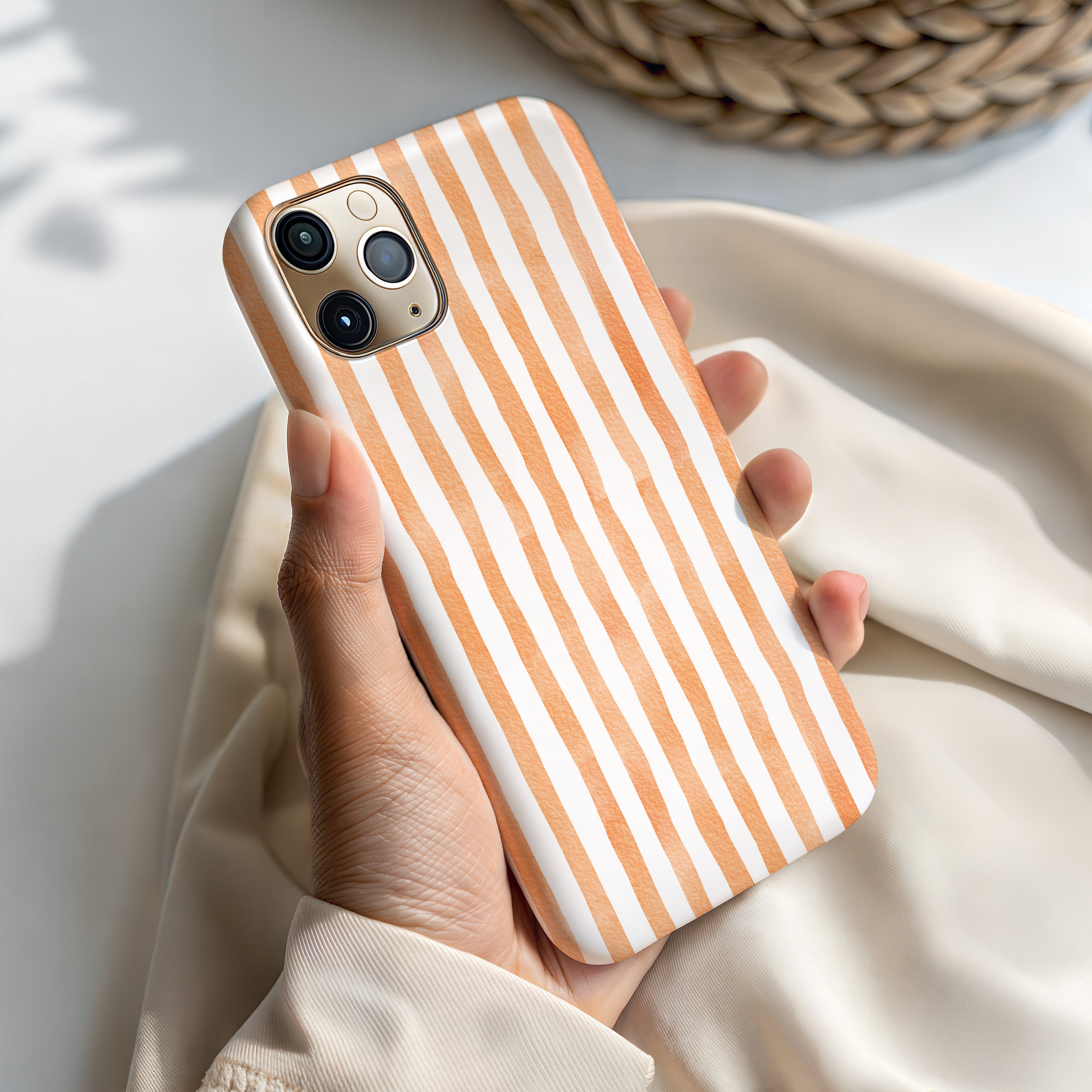 A hand holding a phone case with a striped pattern in shades of orange and white.