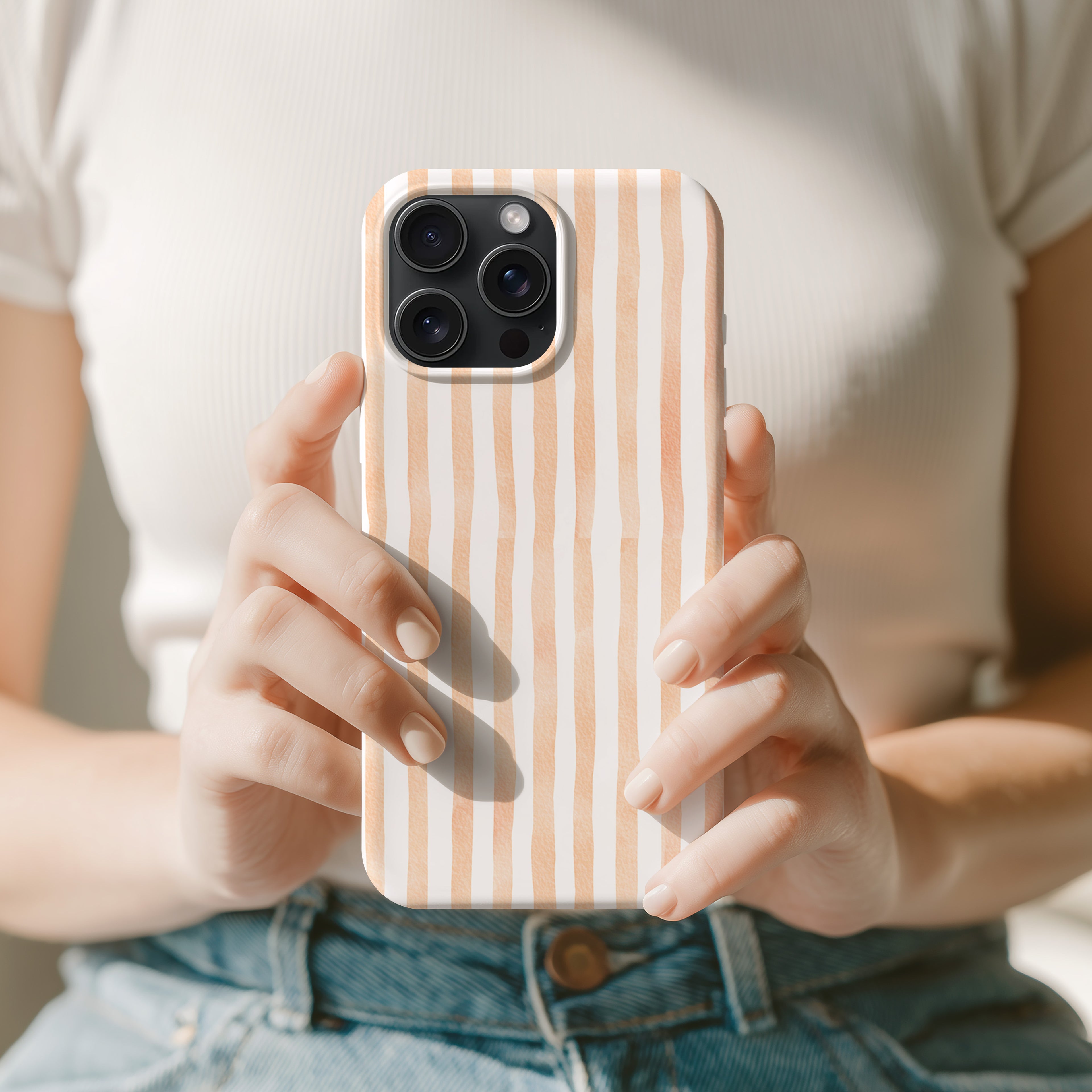A person is holding a smartphone with a striped pattern on the case, wearing a white shirt and blue jeans.