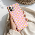 A person's hand holding a pink and white checkered phone case with yellow lemon designs.