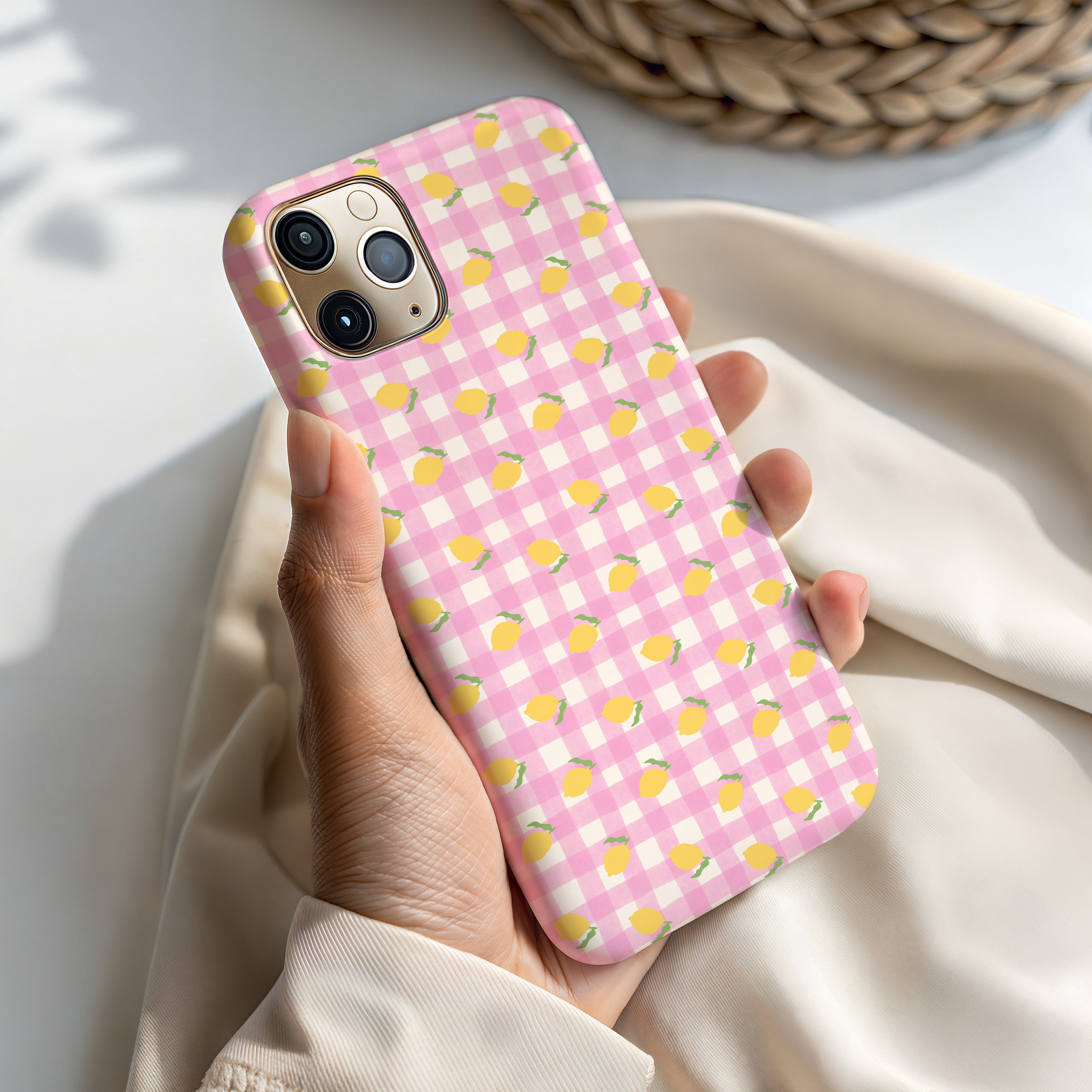 A person's hand holding a pink and white checkered phone case with yellow lemon designs.