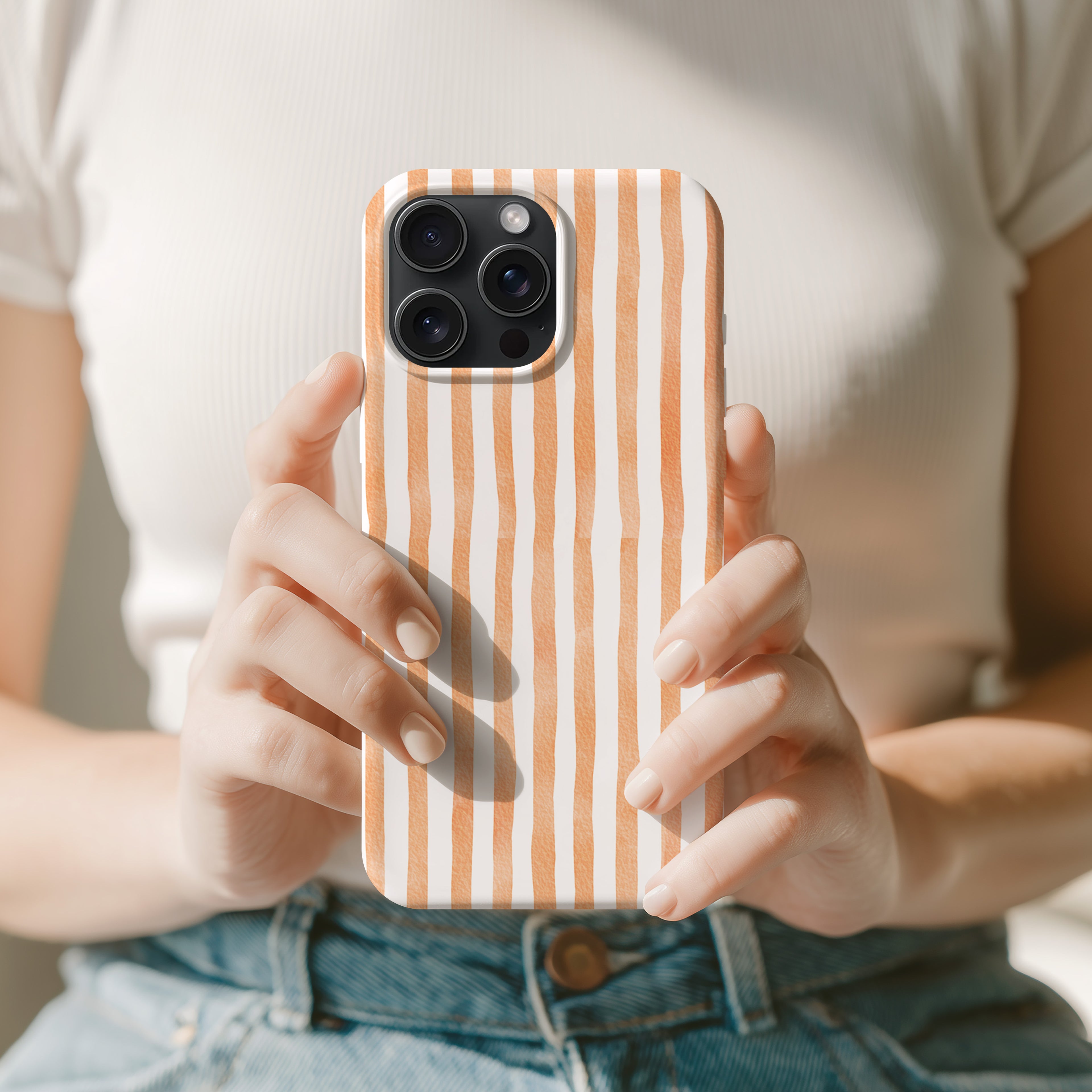 A person is holding a smartphone with a striped pattern on the case, wearing a white shirt and blue jeans.