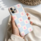 A person's hand holding a phone case with a pattern of blue and white stripes and pink stars.