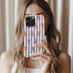 A woman is holding a smartphone with a striped lobster pattern case, taking a selfie in front of a curtain.