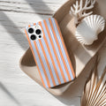 a smartphone with a striped case, placed on a wooden surface alongside a seashell and some dried leaves.