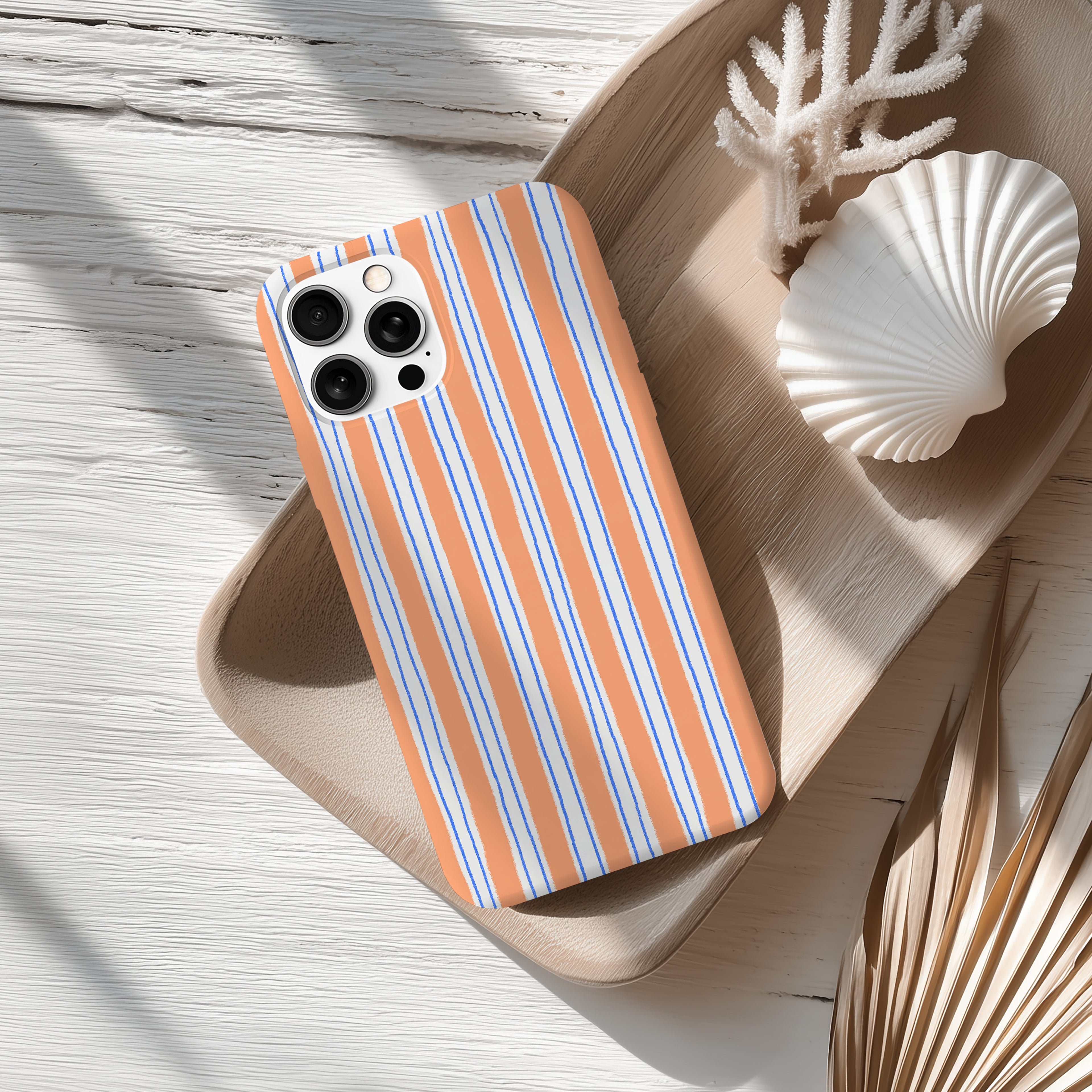 a smartphone with a striped case, placed on a wooden surface alongside a seashell and some dried leaves.