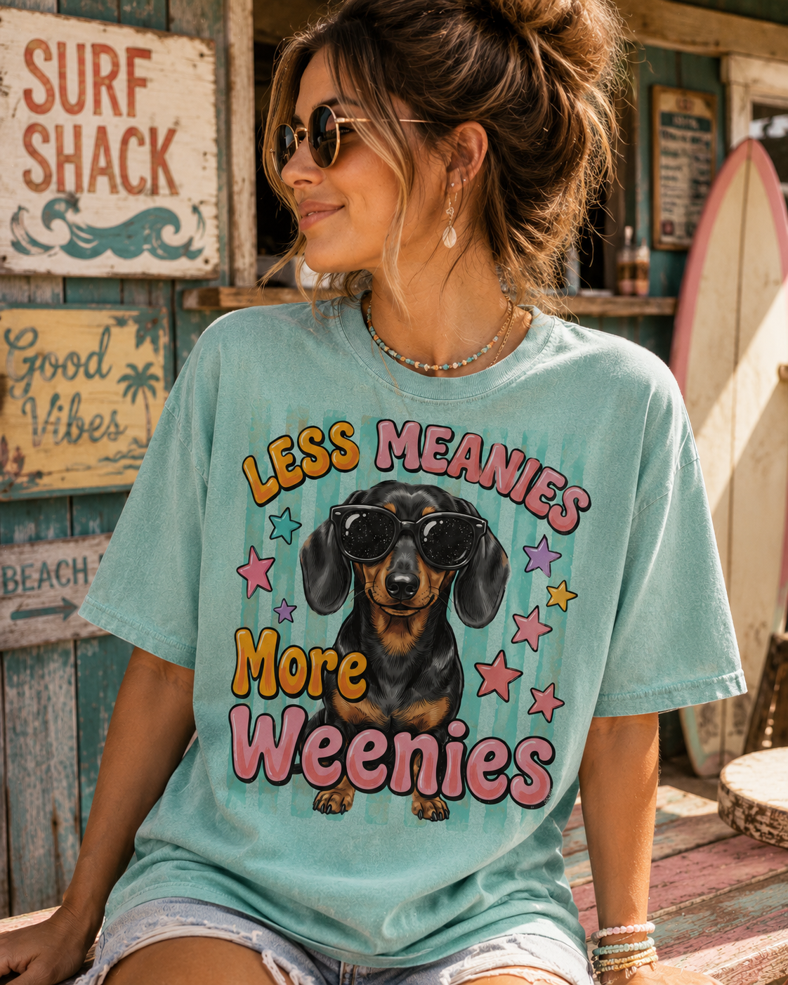 A woman wearing a turquoise t-shirt with a graphic of a dachshund dog and the text "LESS MEANIES MORE WEEENIES" printed on it.