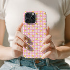 A person is holding a phone case with a pink and yellow checkered pattern.